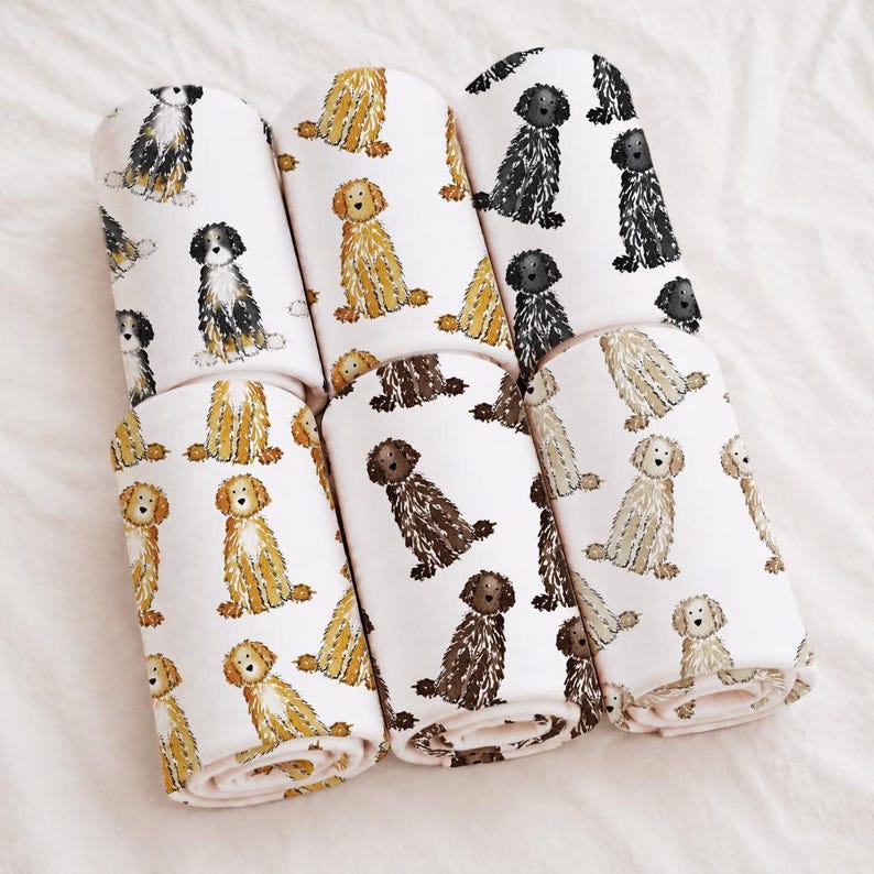 May include: Five rolls of light pink fabric featuring a repeating pattern of illustrated dogs in various colors including black, white, golden, and brown. Each roll displays a different selection of these canine illustrations printed on the surface.