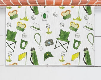 May include: White doormat with a repeating pattern of green golf clubs, golf balls, hats, chairs, and cameras. The doormat has a white background with green, yellow, and brown accents.