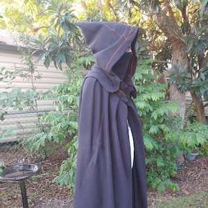 May include: A black hooded cloak with orange stitching along the hood's edge. The cloak is long and flowing, with a matching face covering. The garment is made of a dark fabric, suitable for cosplay or costume events.