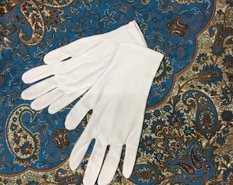 Pode incluir: Um par de luvas de algodão branco. As luvas estão sobre um tecido estampado azul e dourado.