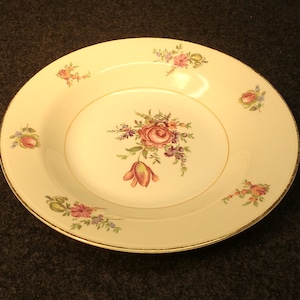 May include: A white ceramic soup bowl with a gold rim and a floral design featuring pink, purple, and green flowers.