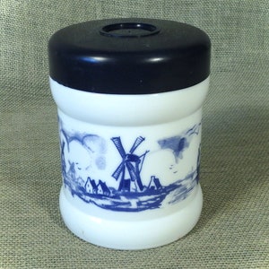 May include: White ceramic jar with a blue and white windmill scene. The jar has a black plastic lid.