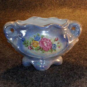 May include: A small, blue and white ceramic planter with a floral design. The planter has a scalloped rim and three feet.