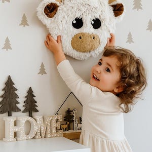 Handmade Highland Cow wall mount made from soft Shaggy Minky fleece in creamy beige with warm brown ears, plush tan horns, and large black felt eyes. Lightweight and gently padded, this 10 x 10 x 3.5 inch piece brings cozy charm and playful character to nursery or toddler room walls. Perfect for Scandi-boho or nature-themed decor, it adds texture and warmth while being safe and easy to hang. Ideal for woodland or farm animal-inspired interiors.
