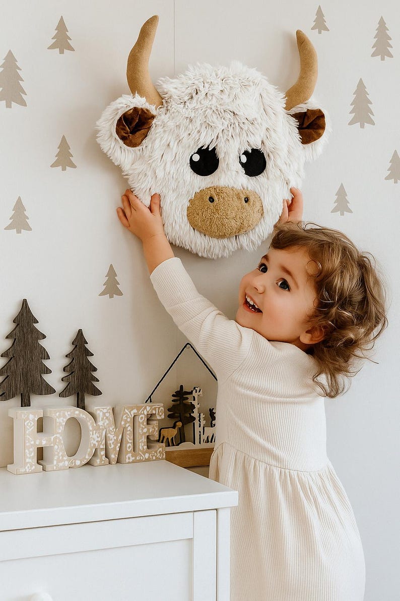 Handmade Highland Cow wall mount made from soft Shaggy Minky fleece in creamy beige with warm brown ears, plush tan horns, and large black felt eyes. Lightweight and gently padded, this 10 x 10 x 3.5 inch piece brings cozy charm and playful character to nursery or toddler room walls. Perfect for Scandi-boho or nature-themed decor, it adds texture and warmth while being safe and easy to hang. Ideal for woodland or farm animal-inspired interiors.