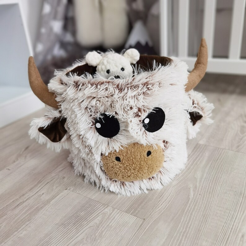 Charming Highland cow toy basket in plush design, perfect for organizing and decorating a child's nursery with a fun and unique touch.