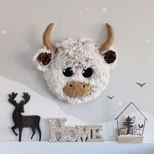 Charming wall-mounted Highland cow head decor, crafted from plush fabric, ideal for enriching nursery walls and complementing a nature-themed kids' room.