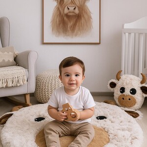 Round Highland Cow nursery rug handmade from soft Shaggy Minky fleece in creamy beige, tan brown, and dark chocolate details. Features a playful 3D cow face with plush ears and nose, black felt eyes, and a cozy, thick pile perfect for tummy time or gentle play. Measures approx. 37 inches and adds a warm, natural texture to the room. Lightweight and baby-safe, this cuddly floor mat is ideal for Montessori spaces, boho nurseries, and photo sessions.