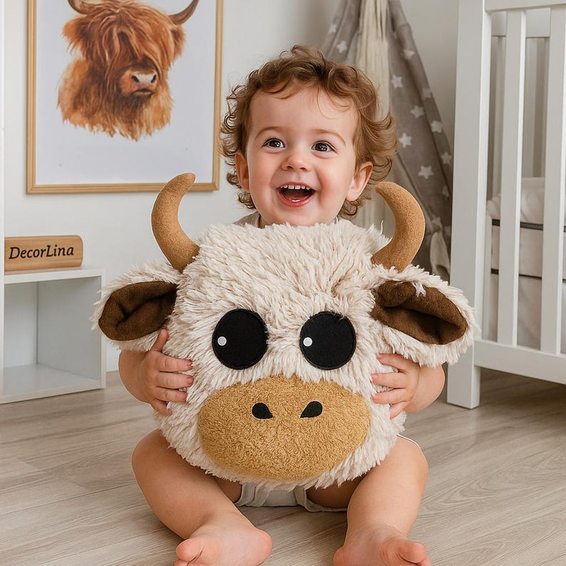 Soft and cozy handmade Highland Cow pillow made from premium shaggy fleece fabric in creamy beige and warm brown tones. Features large black felt eyes, soft plush horns, floppy ears, and a textured, long-pile surface that gives it a cuddly and natural look. Approximately 10 x 10 x 9 inches in size, this plush animal pillow is perfect for nursery decor, toddler snuggles, and photo props. A unique, warm-toned cushion with a charming farm animal design.