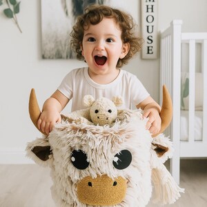 Handmade Highland Cow storage basket crafted from soft Shaggy Minky fleece in creamy beige and tan, featuring 3D plush horns, floppy ears, a textured brown snout, and oversized black felt eyes. Sized approx. 10 x 10 x 9 inches, this lightweight and flexible basket is perfect for holding toys, books, or baby essentials. A playful and functional nursery accessory that adds warmth and personality to farm animal or Scandi-boho themed spaces.