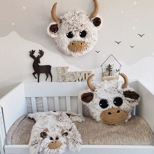 Cozy Highland cow plush pillow displayed in a nursery setting with coordinated decor items like a wall head and lovey, all available for purchase to create a harmonious kids' room theme.