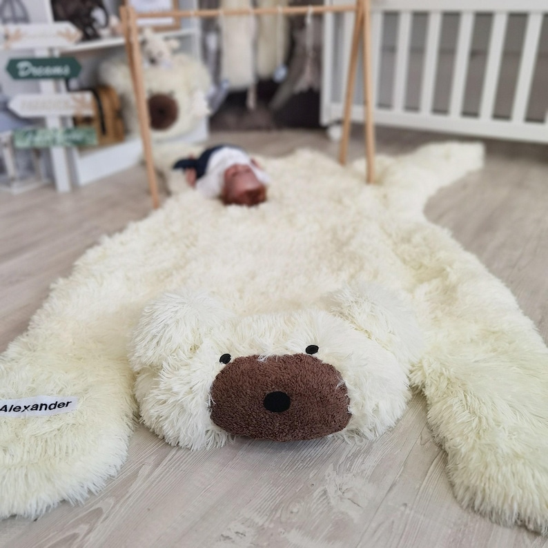 A large white plush polar bear toy is lying on a wooden floor, with a baby sleeping on top of it.