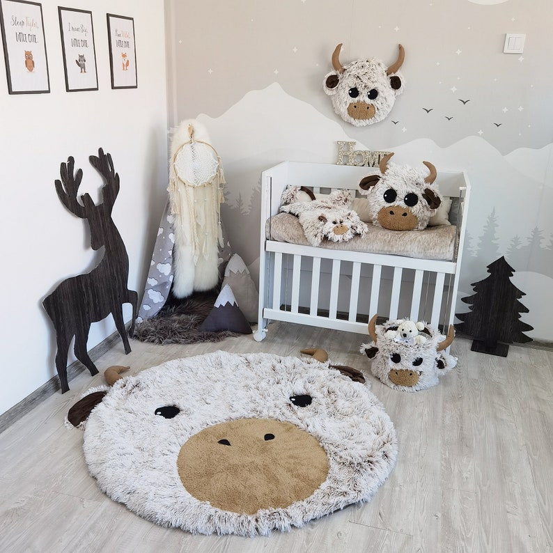 Delightful nursery setup featuring a large Highland cow plush rug, complemented by a matching plush pillow and decorative items, creating a cohesive and enchanting theme for a child's room.