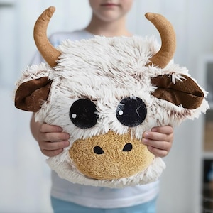 Soft and cozy handmade Highland Cow pillow made from premium shaggy fleece fabric in creamy beige and warm brown tones. Features large black felt eyes, soft plush horns, floppy ears, and a textured, long-pile surface that gives it a cuddly and natural look. Approximately 10 x 10 x 9 inches in size, this plush animal pillow is perfect for nursery decor, toddler snuggles, and photo props. A unique, warm-toned cushion with a charming farm animal design.