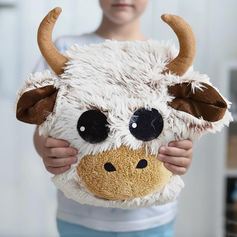 Soft and cozy handmade Highland Cow pillow made from premium shaggy fleece fabric in creamy beige and warm brown tones. Features large black felt eyes, soft plush horns, floppy ears, and a textured, long-pile surface that gives it a cuddly and natural look. Approximately 10 x 10 x 9 inches in size, this plush animal pillow is perfect for nursery decor, toddler snuggles, and photo props. A unique, warm-toned cushion with a charming farm animal design.