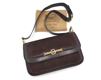 Op de afbeelding: Een bruine suède schoudertas met een gouden ketting en sluiting. De tas heeft een klep sluiting en een klein gouden logo met de tekst "CELINE Paris".