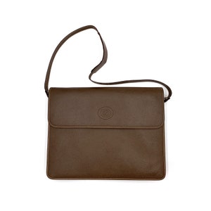 May include: A brown leather shoulder bag with a flap closure and a circular logo on the front.