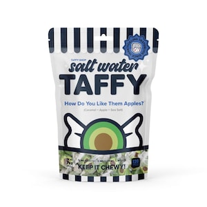 May include: A white bag with a black and white striped design. The bag contains salt water taffy with a green and brown avocado design. The bag says "Salt Water Taffy" and "How Do You Like Them Apples? (Caramel + Apple + Sea Salt)". The bag also says "Keep It Chewy!" and "7oz (198g)".