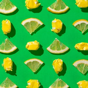 K&ouml;nnte beinhalten: Eine flache Anordnung von gelben Zitronenscheiben und gelben Bonbons auf gr&uuml;nem Hintergrund. Die Zitronenscheiben sind in einem Muster angeordnet, wobei die Bonbons zwischen ihnen verstreut sind.