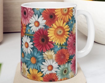 Könnte beinhalten: Weiße Keramiktasse mit einem bunten Blumenmuster, das verschiedene Gänseblümchen in Rot-, Orange-, Gelb-, Rosa-, Blau- und Weißtönen zeigt. Die Tasse hat einen Henkel und steht auf einem beigefarbenen Untersetzer.