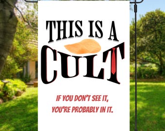 Op de afbeelding: Witte tuin vlag met de tekst "THIS IS A CULT" in zwart, met een cartoon oranje haar en rode stropdas afbeelding. De vlag bevat ook de tekst "IF YOU DON'T SEE IT, YOU'RE PROBABLY IN IT."