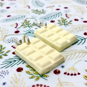 May include: A pair of white chocolate bar earrings with silver hooks. The earrings are made of polymer clay and are shaped like a chocolate bar with squares.