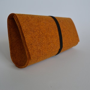 May include: A brown felt clutch with a black strap. The clutch is made of a soft, textured material.