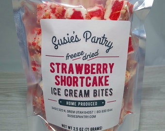 Könnte beinhalten: Ein transparenter Plastikbeutel gefüllt mit gefriergetrockneten Erdbeer-Shortcake-Eis-Bissen. Der Beutel hat ein Etikett mit der Aufschrift "Susie's Pantry" und "freeze dried Strawberry Shortcake Ice Cream Bites". Das Etikett enthält auch die Website und die Kontaktinformationen des Unternehmens.