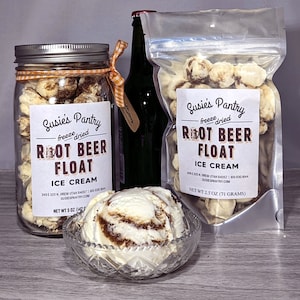 May include: A clear glass jar filled with freeze-dried root beer float ice cream. The jar has a white label with the text "Susie's Pantry freeze dried Root Beer Float Ice Cream" and the net weight of 5 ounces. A clear plastic bag filled with freeze-dried root beer float ice cream. The bag has a white label with the text "Susie's Pantry freeze dried Root Beer Float Ice Cream" and the net weight of 2.5 ounces. A scoop of vanilla ice cream with swirls of chocolate.