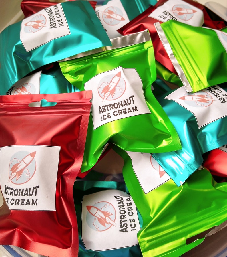 Pu&ograve; includere: Un mucchio di sacchetti di alluminio colorati di gelato per astronauti. I sacchetti sono in tonalit&agrave; di rosso, verde e verde acqua. Ogni sacchetto ha un'etichetta bianca con le parole "Astronaut Ice Cream" e una grafica di razzo.