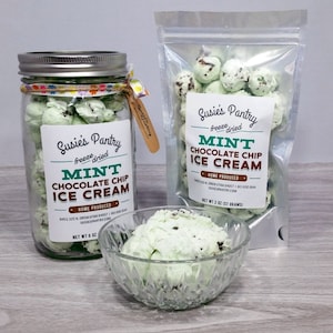 May include: A clear glass jar filled with freeze-dried mint chocolate chip ice cream. The jar has a silver lid and a label that reads "Susie's Pantry freeze dried Mint Chocolate Chip Ice Cream Home Produced".