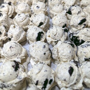 Pu&ograve; includere: Primo piano di molte palline di gelato dall'aspetto cookies and cream. Il gelato &egrave; bianco con pezzi di biscotti scuri. Le palline sono disposte vicine, suggerendo una produzione artigianale.