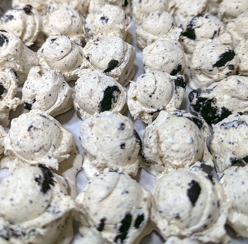 Pu&ograve; includere: Primo piano di molte palline di gelato dall'aspetto cookies and cream. Il gelato &egrave; bianco con pezzi di biscotti scuri. Le palline sono disposte vicine, suggerendo una produzione artigianale.
