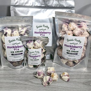 K&ouml;nnte beinhalten: Drei durchsichtige Plastikt&uuml;ten gef&uuml;llt mit gefriergetrockneter Heidelbeer-Kuchen-Eiscreme. Die Beutel sind mit "Susie's Pantry Freeze Dried Huckleberry Pie Ice Cream" beschriftet.