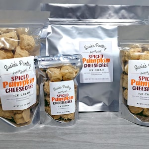 May include: Several clear, sealed bags of freeze-dried spiced pumpkin cheesecake ice cream. The bags vary in size and contain beige, spherical pieces. Each bag has a white label with the text "Susie's Pantry" and "Spiced Pumpkin Cheesecake Ice Cream."