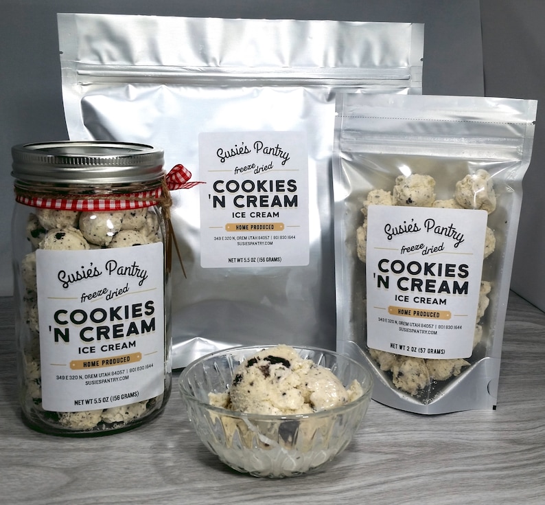 Pu&ograve; includere: Un assortimento di prodotti di gelato Cookies 'N Cream liofilizzato. L'immagine mostra un barattolo di vetro, due buste argentate e una piccola ciotola di vetro piena di gelato. Ogni contenitore ha un'etichetta con il testo "Susie's Pantry Cookies 'N Cream Ice Cream".