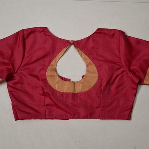 May include: A red sleeveless blouse with a gold trim around the neckline and sleeves. The back of the blouse has a keyhole opening with a gold trim.