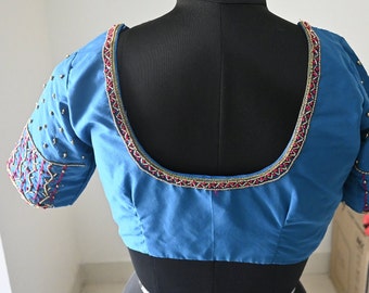 Op de afbeelding: Een blauwe, mouwloze blouse met een kraag van kralen en kralenversieringen op de mouwen.