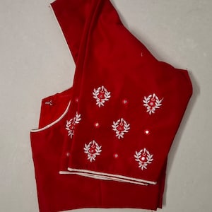 Puede incluir: Una blusa roja sin mangas con bordados blancos y pequeños espejos redondos.