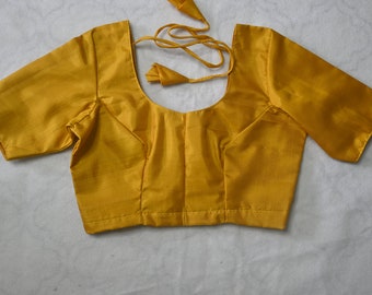 May include: A mustard yellow sleeveless blouse with a scoop neck and short sleeves. The blouse has a tie at the back.