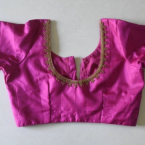 Puede incluir: Una blusa magenta sin mangas con un escote de cuentas doradas y ribetes dorados en las mangas.