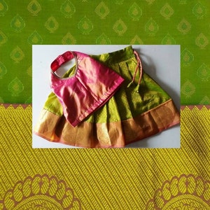 May include: A green and pink traditional Indian outfit for a young girl. The skirt is green with gold trim and the top is pink with a halter neck style.