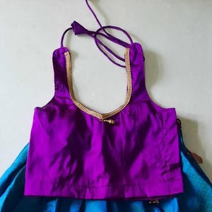 May include: A purple sleeveless blouse with a gold trim and a gold tassel. The blouse is made of a silky fabric.