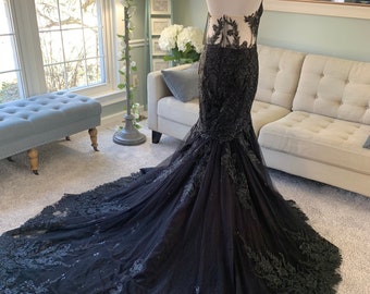 Puede incluir: Un vestido de novia de sirena de tul y encaje negro con escote de corazón y un corpiño transparente. El vestido presenta intrincados bordados florales y una larga cola.