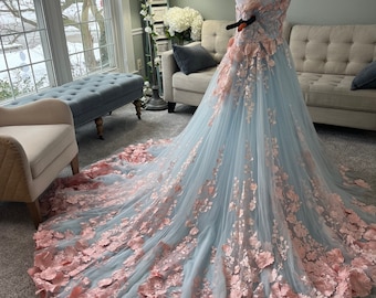 Puede incluir: Un vestido de tul azul claro con un corpiño ajustado y una falda completa. El vestido está adornado con delicados apliques florales de color rosa.