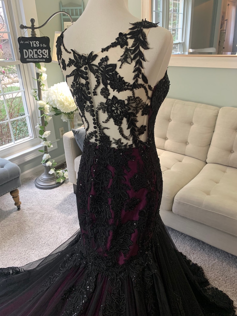 May include: A black and burgundy mermaid style gown with black lace and beading. The gown has a sheer bodice with a lace overlay and a fitted skirt.