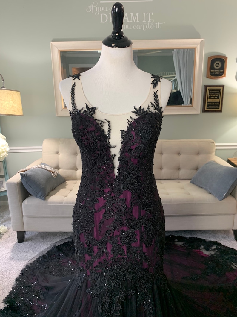 May include: A black and purple mermaid-style gown with black lace detailing and a sheer bodice. The gown has a fitted silhouette and a flowing skirt.