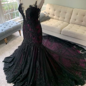 May include: A black and burgundy mermaid-style gown with intricate lace detailing and a sheer bodice.