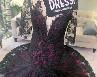 May include: A black and purple wedding dress with lace detailing. The dress has a fitted bodice and a flowing skirt. A sign says "She said YES to the DRESS! #bridesandtailor"