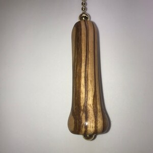 K&ouml;nnte beinhalten: Ein Holz-L&uuml;fterzug mit einem braunen und hellbraunen Streifenmuster. Der Zug hat eine goldene Kette und eine goldene Kugel oben und unten.